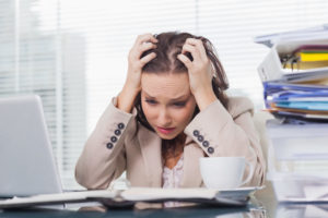 Woman holding her head looking stressed with stacks of paperwork